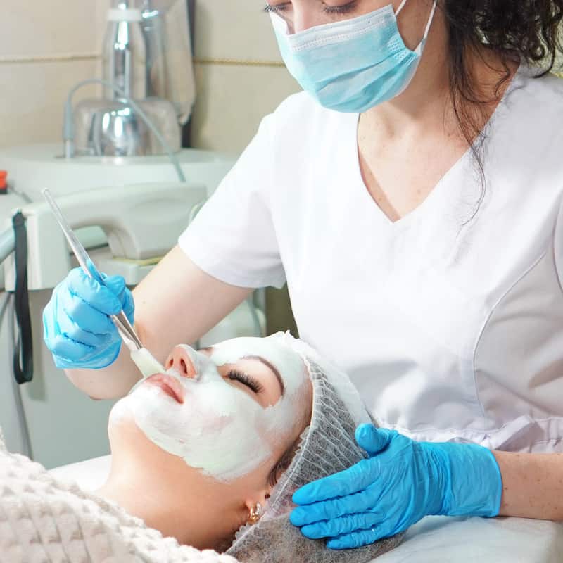 Cosmetologist doing cosmetic face mask treatment for the young woman.