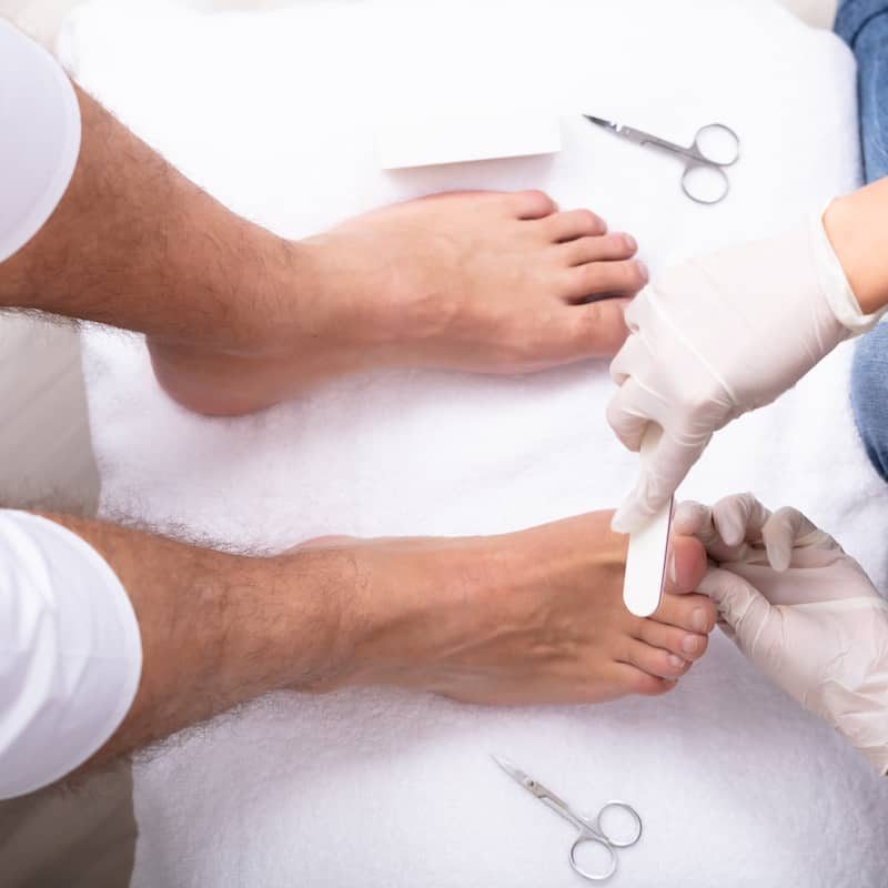 High Angle View Of Beautician Filling Man's Nail In Salon